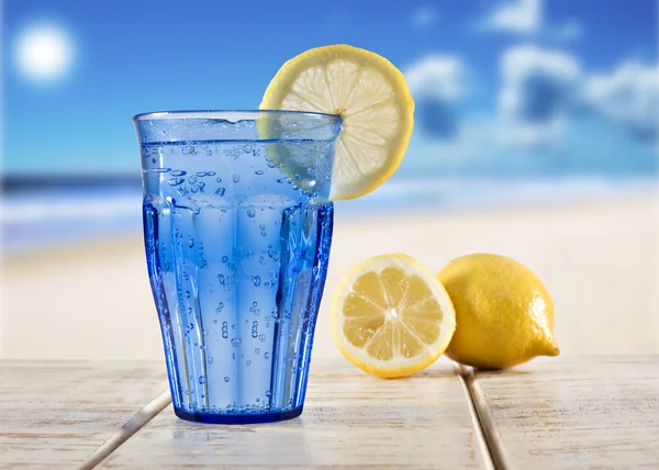 与苏打水和柠檬俯瞰热带海滩木甲板上的蓝色玻璃 — 图库照片