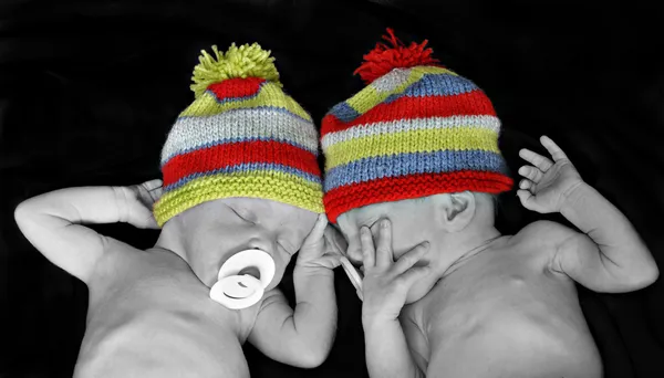 New born twins with colorful striped hats — Stock Photo, Image