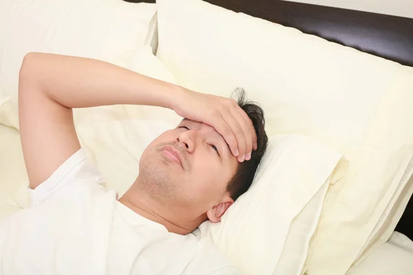 Закрытие лежащего в постели молодого человека, принимая температуру и час — стоковое фото