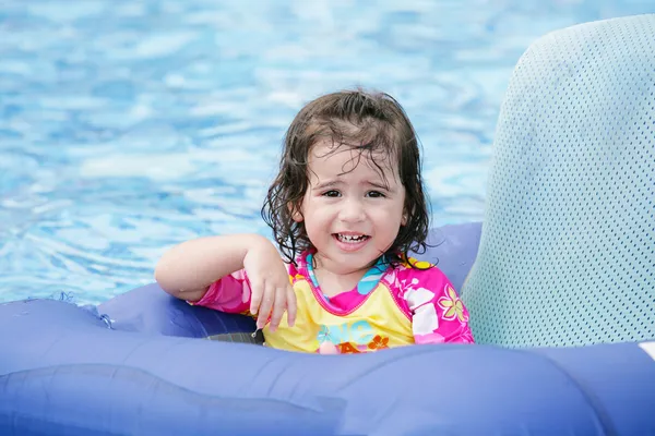 Малышка развлекается на голубом поплавке в тропическом бассейне — стоковое фото