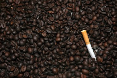 Cigarette butts off on a bunch of fried coffee beans are used as an ashtray clipart