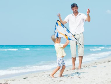 Boy with father on beach playing with a kite clipart