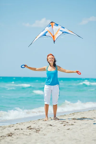 Frau am Strand spielt mit einem bunten Drachen — Stockfoto