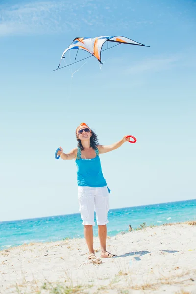 Frau am Strand spielt mit einem bunten Drachen — Stockfoto