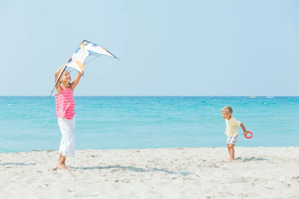 Flicka med bror på stranden spelar med en drake — Stockfoto