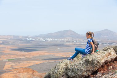 Girl sitting on cliff's edge, looking to a sky clipart