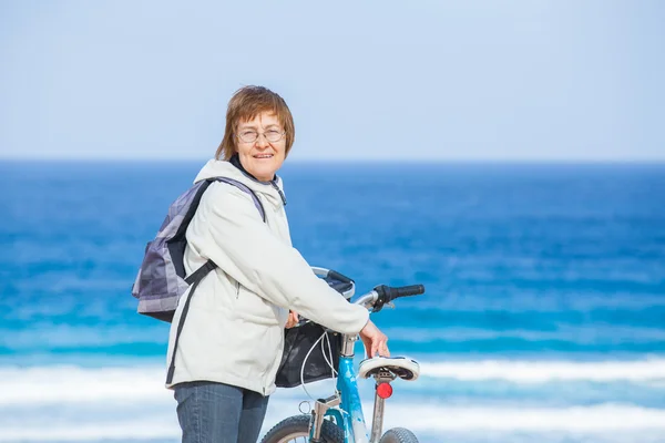 En trevlig äldre dam cykla på stranden. — Stockfoto