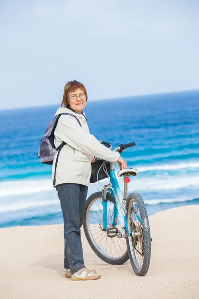 资深美女在沙滩上骑一辆自行车. — 图库照片
