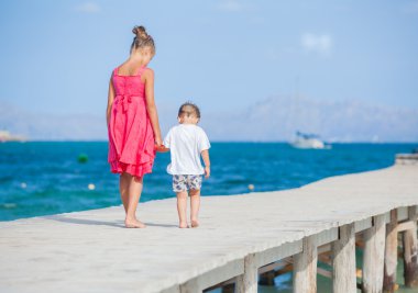 Girl with her brother walking on jetty clipart