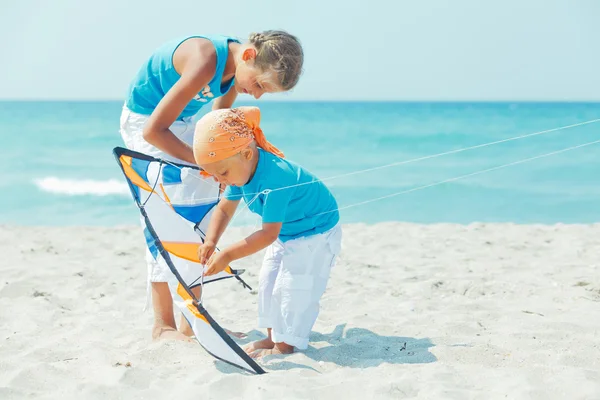 Pojke med syster på stranden spelar med en drake — Stockfoto