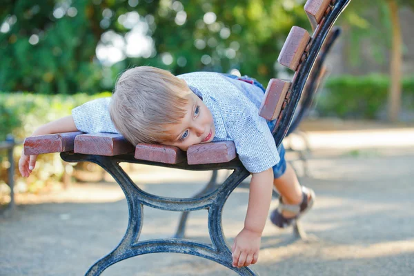Söt liten pojke avkopplande på bänken i en stad — Φωτογραφία Αρχείου