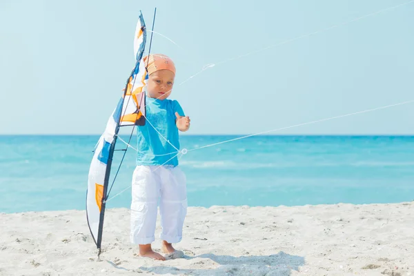 Rapaz bonito na praia brincando com um papagaio colorido — Fotografia de Stock