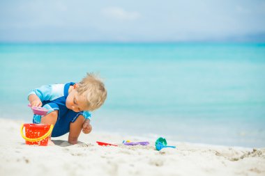 Boy playing with beach toys on tropical beach clipart