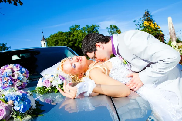 Noivo e noiva beijando em um capuz de carro — Fotografia de Stock