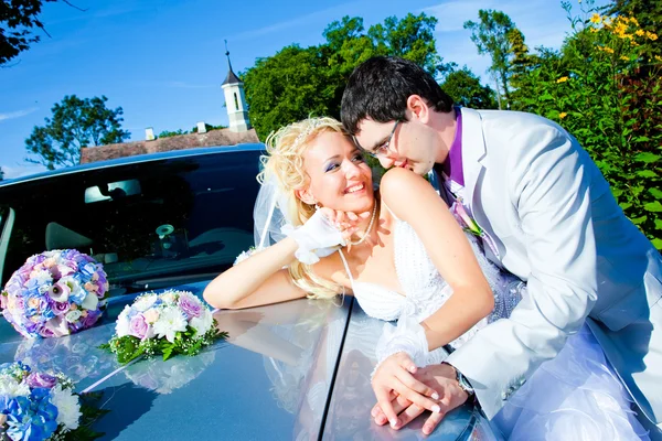 Groom and bride kissing on a car cowl — Stock Photo, Image