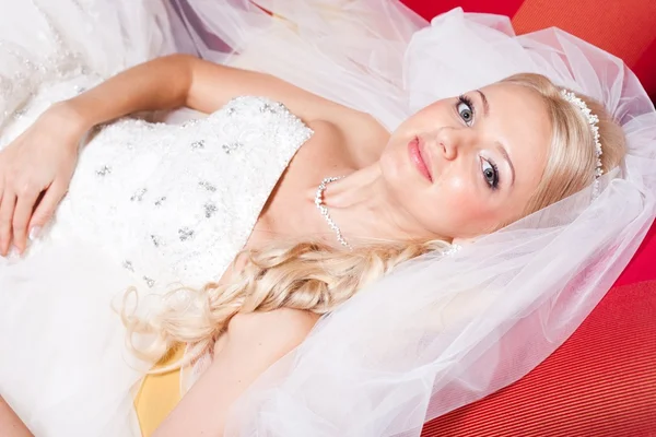 Beautiful bride lying on red sofa — Stock Photo, Image