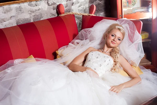 Schöne Braut auf rotem Sofa liegend — Stockfoto