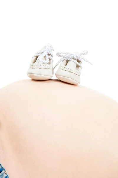 Vientre de la mujer embarazada con botas pequeñas en blanco aislado —  Fotos de Stock