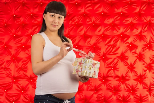 Retrato de una joven embarazada con un regalo en un fondo rojo —  Fotos de Stock