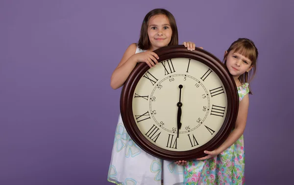 Büyük duvar saati tutan iki kız — Stok fotoğraf