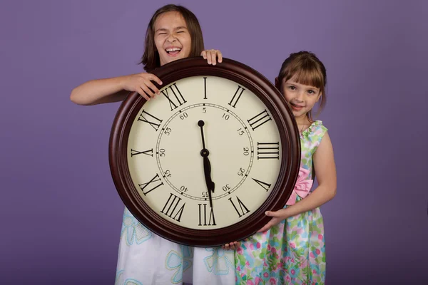 大きな壁時計を保持している 2 つの笑っている女の子 — ストック写真