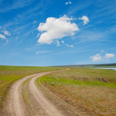 Winding rural road to horizon under cloudy sky clipart