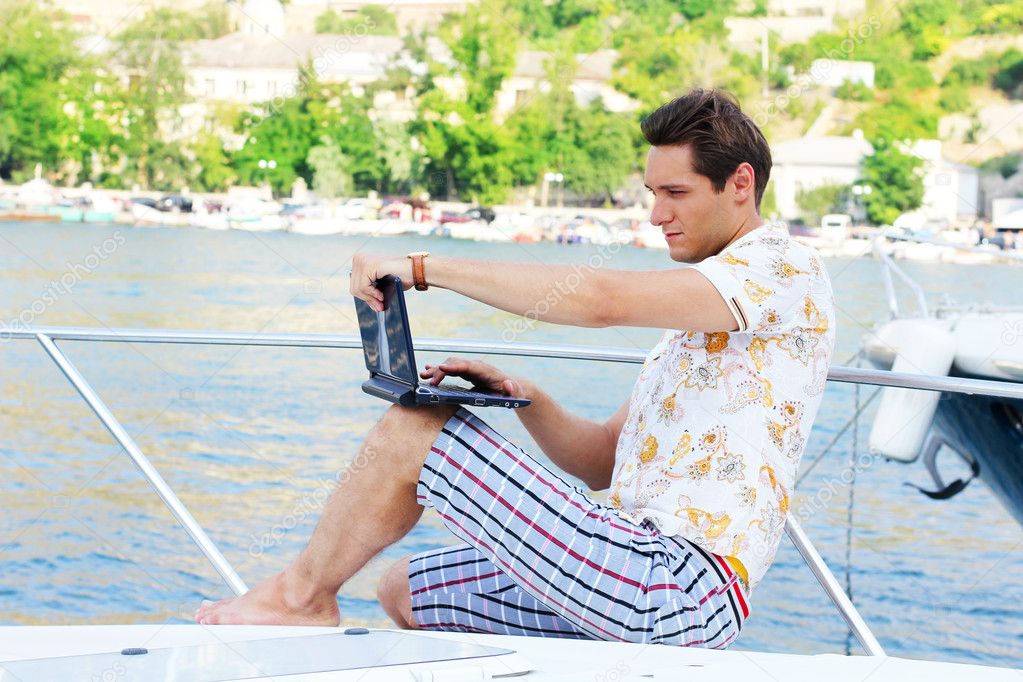 Working man with laptop sitting on white yacht, beach