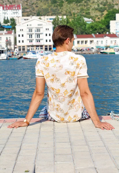 Knappe man ontspannen, zittend op de pier in de buurt van zee, op zoek awa — Stockfoto