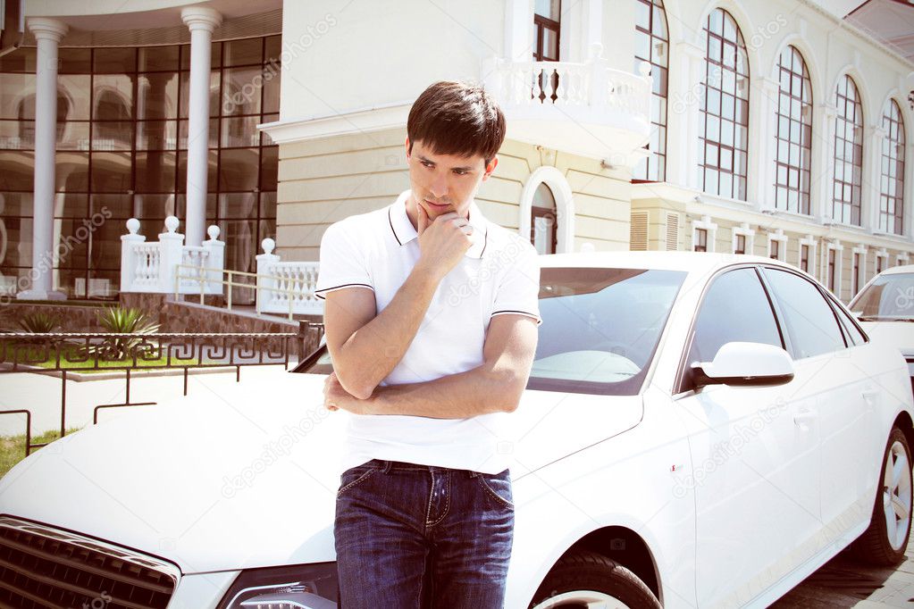 Handsome man casually leaning against the white car at office building background