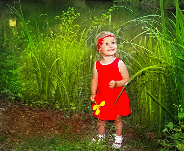 Boldog mosolygó kis móka lány piros ruha, virág a kezében, zöld szabadban — Stock Fotó