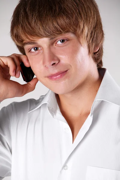 Улыбающийся молодой человек разговаривает по мобильному телефону с копировальным пространством, студент — стоковое фото