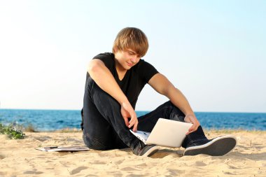 Young student man using laptop on the beach clipart