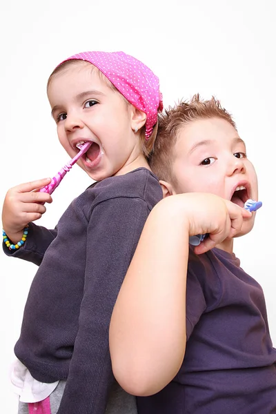 Um menino e uma menina adoráveis escovando os dentes no fundo branco — Fotografia de Stock