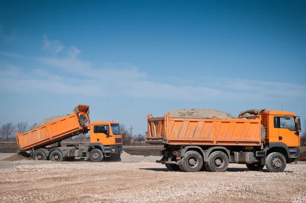 O caminhão laranja descarregando areia no local — Fotografia de Stock