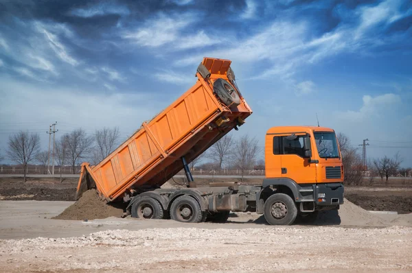De oranje vrachtwagen lossen zand op de site — Stockfoto