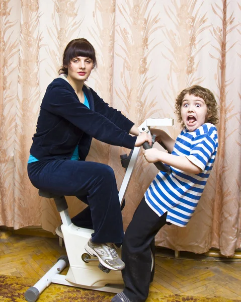 母亲和儿童自行车训练器上 — 图库照片