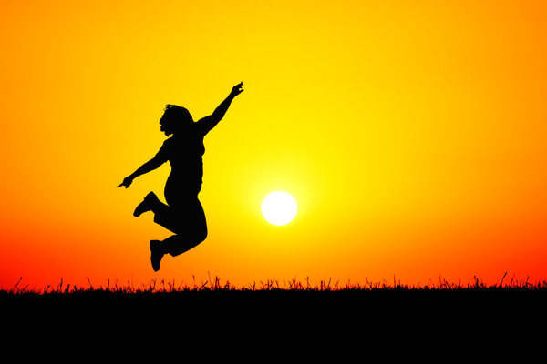 A girl jumping up in the air on top of a hill in front of a blood red sunset