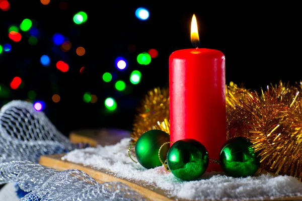 Красная свеча с зеленым новогодним мячом на фоне огней — стоковое фото