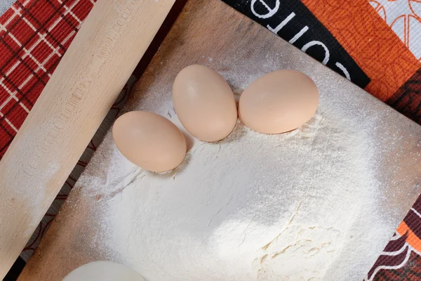 Three chicken eggs on a cutting board with flour — Stock Photo, Image