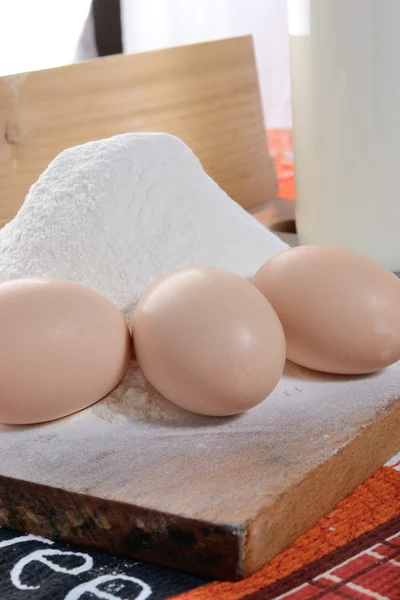 Trois œufs de poulet sur une planche à découper avec de la farine — Photo