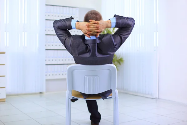 Деловой человек, откинувшись на спинку стула, расслабляется на белом фоне — стоковое фото
