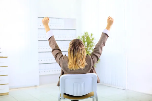 Biznes kobieta siedzi na krześle i z jej ręce w powietrzu świętować sukces — Zdjęcie stockowe