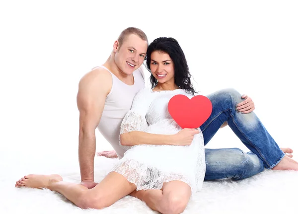 Beautiful young love couple sitting on the floor with a big red heart — Stock Photo, Image