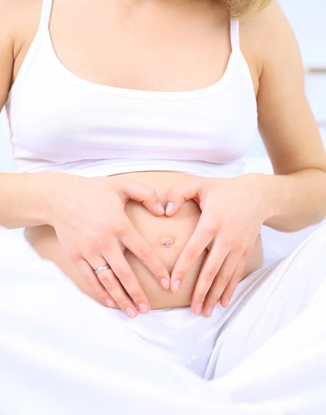 Pregnant woman making heart shape with hands over her stomach — Stock Photo, Image