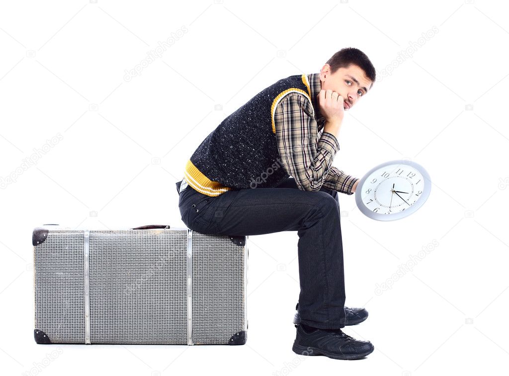 Young man waiting at airport, holding big clock, isolated over white
