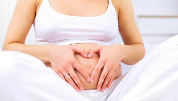 Femme enceinte faisant forme de coeur avec les mains sur son estomac Photos De Stock Libres De Droits