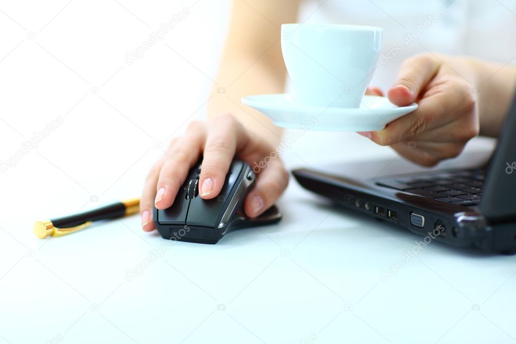 Close-up of businesswoman's hand on mouse and cup of coffee