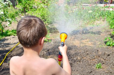 Çocuk bir hortum ile bahçede bitkilerin sulama
