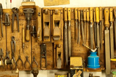 Assortment of do it yourself tools hanging in a wooden cupboard against a wall clipart