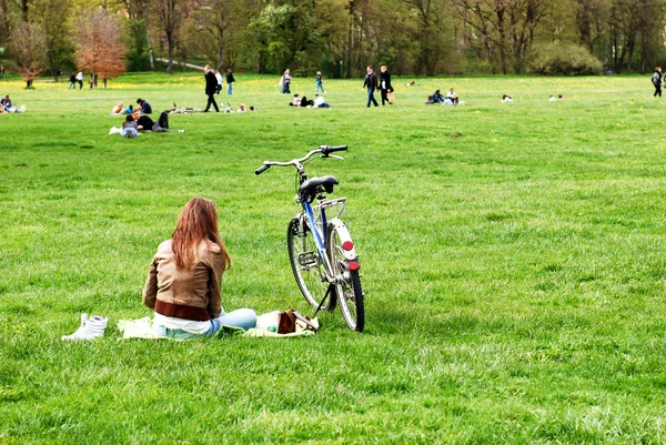 Mooi meisje met een fiets berust op een gras op het stadspark — Stockfoto